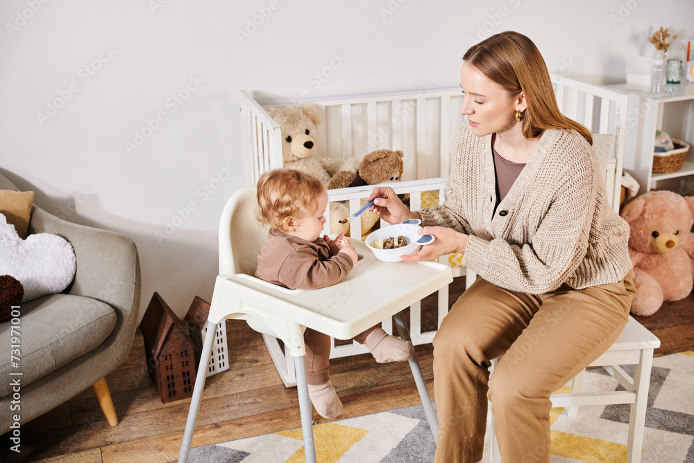 caring woman feeding baby boy with breakfast on baby chair in nursery room, blissful motherhood caring woman feeding baby boy with breakfast on baby chair in nursery room, blissful motherhood