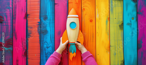 Launch of a red rocket on colorful wooden background, made of wood, held by children's hands. Successful start concept.