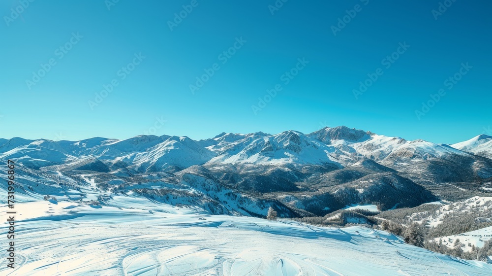 Wide panoramic view of a snow-covered mountain range with clear skies and deep valleys.