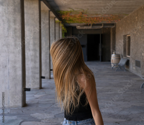 Creative portrait fo a young woman in a concrete outdoor corridor, moving her brown hair.  © Gonzalo