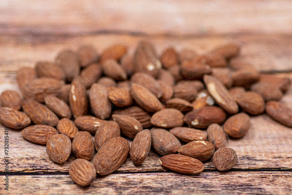 Close up roasted organic brown almond seed on wooden table and some of almond in white porcelain cup Close up roasted organic brown almond seed on wooden table and some of almond in white porcelain cup