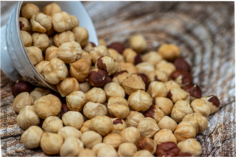 Peeled and roasted organically grown hazelnuts spilling out of a ceramic bowl on wooden table, close-up of healthy roasted hazelnuts, healthy snacks Peeled and roasted organically grown hazelnuts spilling out of a ceramic bowl on wooden table, close-up of healthy roasted hazelnuts, healthy snacks