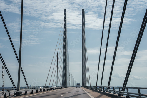 Modern Oresund Bridge connecting Copenhagen and Malmo, viewed from the deck with tall pylons, multiple cables, lane markings, and safety barriers under a partly cloudy sky.