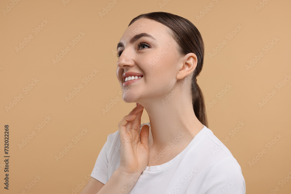 Smiling woman touching her neck on beige background Smiling woman touching her neck on beige background