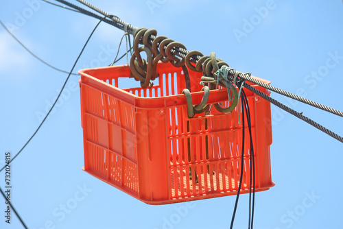 Improvised rectangular red plastic basket hanging from the ropes of a old fishing boat photo