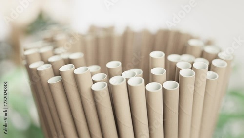Close-up of a bundle of beige paper straws with selective focus, set against a blurred green plant background, signifying eco-friendly alternatives. photo