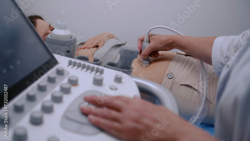 Doctor using sonography machine with digital monitor. Medical specialist conducts ultrasound diagnostic to pregnant female patient. Modern clinic with advanced equipment. Healthcare concept. Close up.