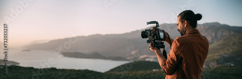 A young Caucasian man with a professional camera in his hands on a mountain by the sea. photo