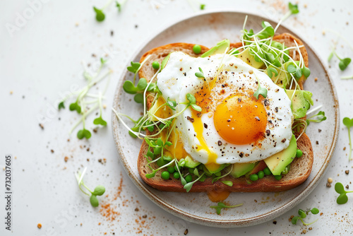 Whole wheat toasted bread with avocado, poached egg, pea sprouts and cheese over white background