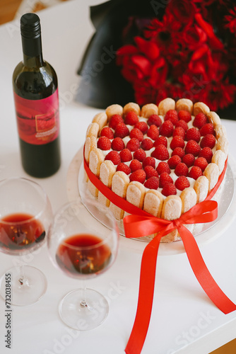 Valentines cake with raspberry on a plate with red wine and glasses on romantic flowers background. Beautiful sweet with fresh berries as a symbol of love for St Valentine's day