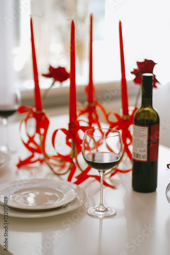 Wine and glasses for the date on white table decorated with red candles and roses. St Valentine's day celebration