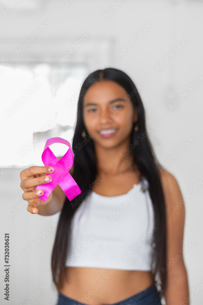young latin brunette woman holding in her hand a pink ribbon symbol of the fight against breast cancer young latin brunette woman holding in her hand a pink ribbon symbol of the fight against breast cancer