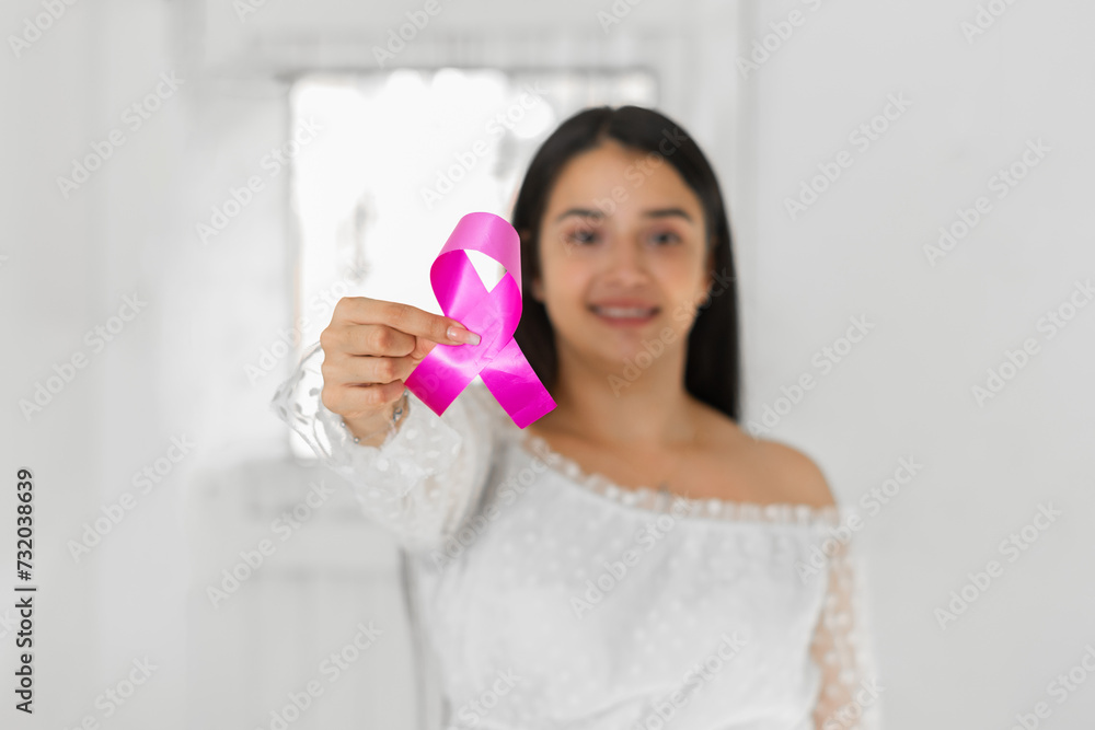 latina woman holding a pink ribbon, symbol against breast cancer, on a blurred white background and smiling. latina woman holding a pink ribbon, symbol against breast cancer, on a blurred white background and smiling.