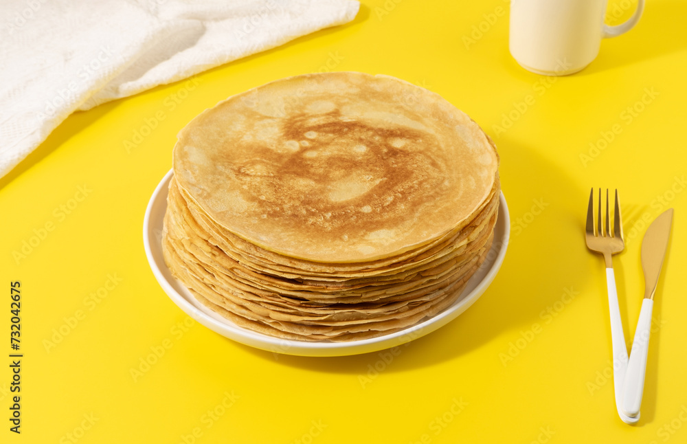 A stack of thin pancakes on a yellow table A stack of thin pancakes on a yellow table