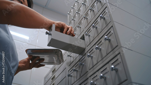 Asian nurse puts samples with blood tests or histology biological tissues analysis in medical metal storage cabinet with racks. Female scientist, microbiologist works in modern scientific laboratory.