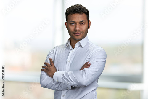 Portrait of young handsome businessman with arms crossed posing on blurred background. Attractive male ceo looking at camera.
