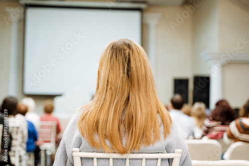 Attentive Woman At Seminar Watches Presentation On Large Screen In Conference Hall