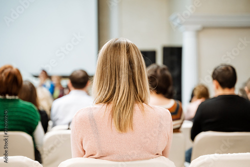 Blonde woman in pink sweater sitting in conference room with audience