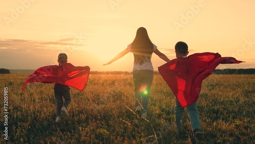 Mom, Super kids dream of becoming superhero, flying in red cape. Mother daughter, son play superheroes in park. Mom child run in red raincoats, have fun outdoor. Family Carnival in sun, Halloween, sky