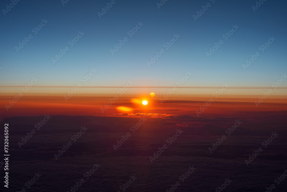 Aerial view of a sunrise with a sunburst effect, featuring a gradient blue sky and clouds lit with fiery orange and red hues, likely taken en route to or from Istanbul.