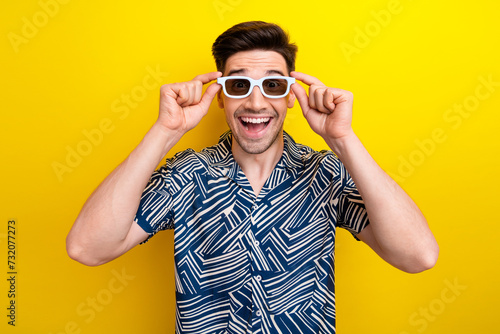 Photo of funky positive man dressed print shirt hands touching 3d glasses staring at amazing film isolated on yellow color background © deagreez