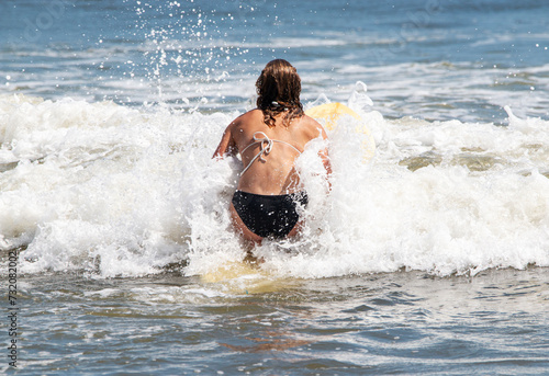 Girl in a bikini on her knees on a surfboard trying to paddle out past the surf © coachwood