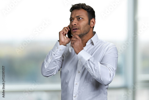 Serious handsome businessman talking on mobile phone with client. Blur window in the background.
