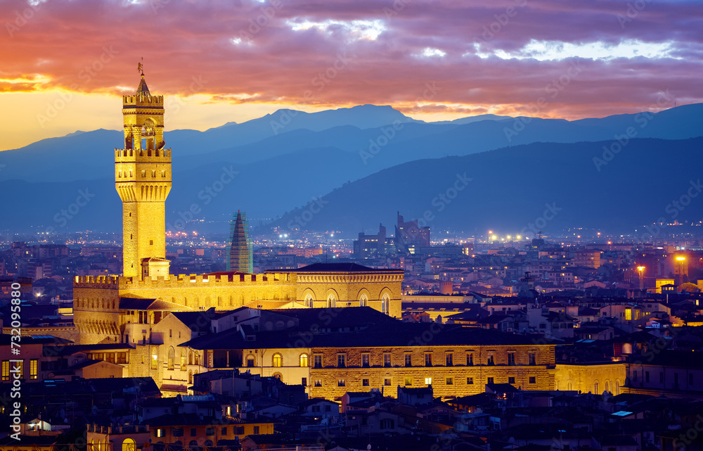 Florence, Tuscany, Italy. Tower of Palazzo Vecchio at night with clouds on the blue dramatic sky after sunset. Firenze evening illumination ancient walls.