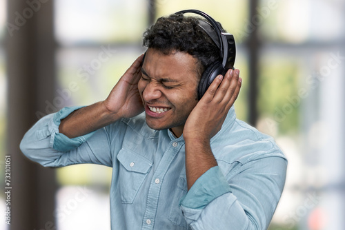 Young expressive man listening to music with headphones. Interior blur background.