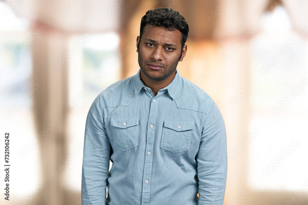Portrait of upset young indian man looking at camera. Disappointed guy on blur interior background. Portrait of upset young indian man looking at camera. Disappointed guy on blur interior background.