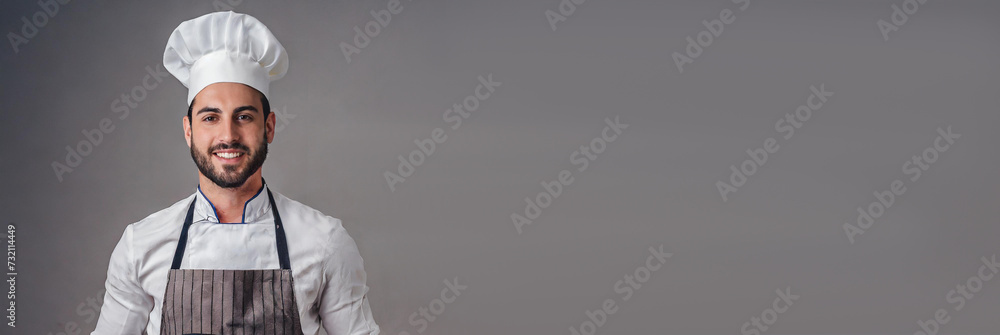 Naklejka premium Panoramic portrait of male chef in apron and hat, isolated on grey background with large copy space for text