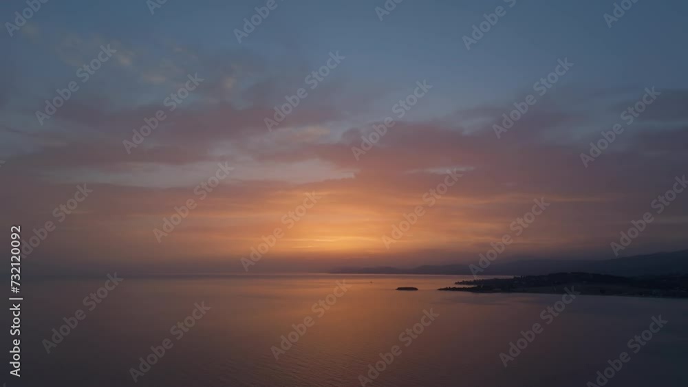A drone ascends capturing the expansive view of a tranquil bay at sunset, with rich gradients from orange to deep blue across the vast sky and reflective sea A drone ascends capturing the expansive view of a tranquil bay at sunset, with rich gradients from orange to deep blue across the vast sky and reflective sea