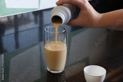 Oral enteral nutrition in a bottle in a woman’s hand in the kitchen. Woman filling a cup with oral enteral nutrition supplementation.  