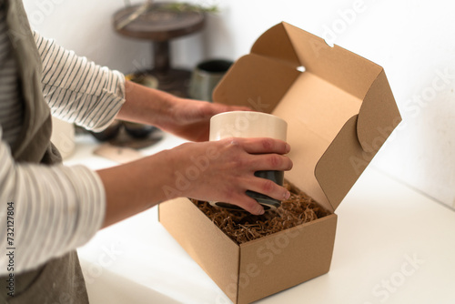 Artisan placing a ceramic vase into a cardboard box with protective packing material for safe transport.