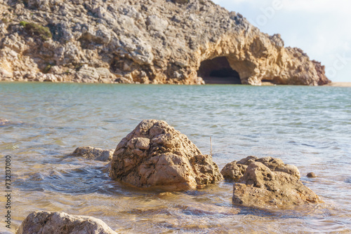 Stones in front of a cave at Praia das Furnas beach with sea water, Algarve, Portugal.