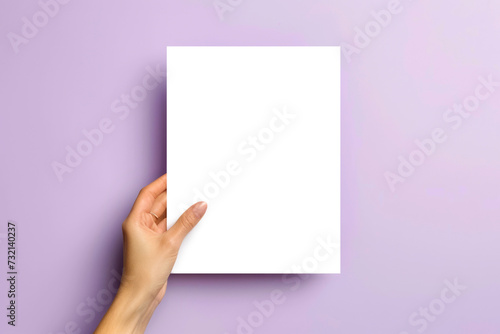 a blank paper mockup. one sheet in the woman hand blank white vertical oriented, on soft violet color background, flatlay.