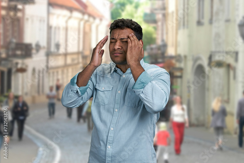 Tired indian man suffering from headache standing outdoors. Health problem concept.