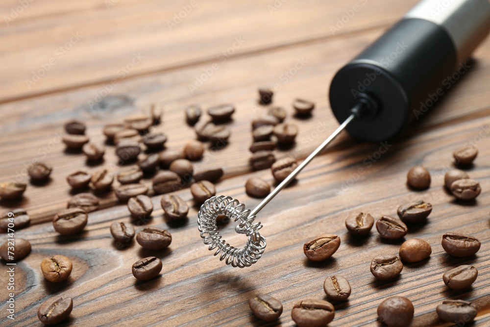 Black milk frother wand and coffee beans on wooden table, closeup Black milk frother wand and coffee beans on wooden table, closeup