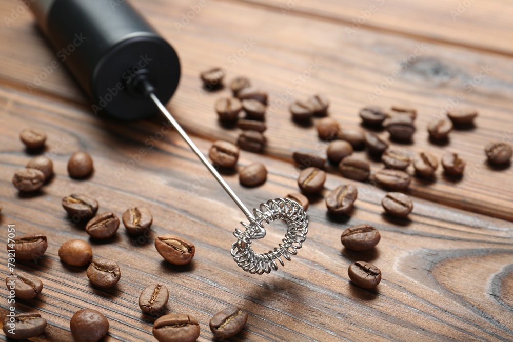 Black milk frother wand and coffee beans on wooden table, closeup Black milk frother wand and coffee beans on wooden table, closeup