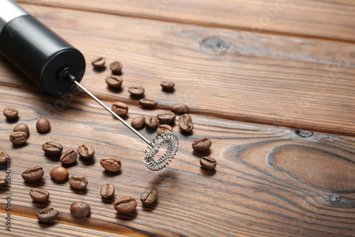 Black milk frother wand and coffee beans on wooden table, closeup. Space for text
