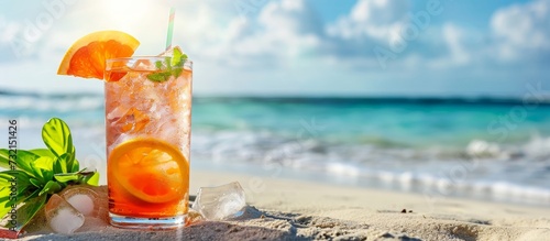 A glass of orange juice rests on the sandy beach, reflecting the vibrant sky and mixing with the flowing water.