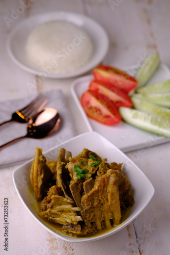 Tengkleng Kambing is is a traditional Central Javanese dish made from young goat bones, with spices, soy sauce, chili. served in a white ceramic bowl on a white wooden table. Indonesian food.  photo