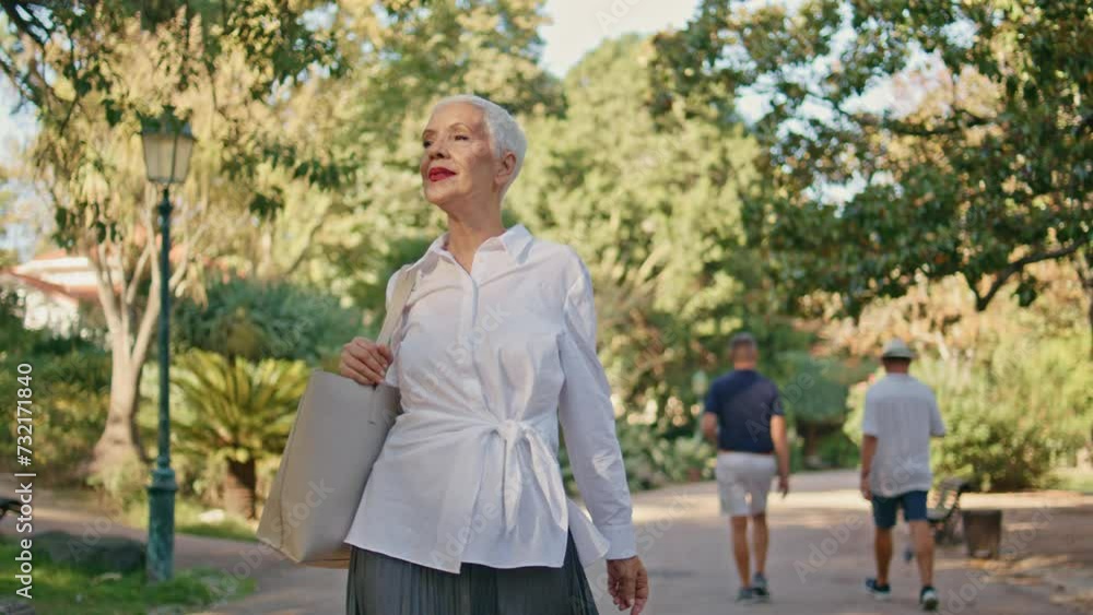 Elderly woman going park path in sunlight. Smiling relaxed senior resting alone Elderly woman going park path in sunlight. Smiling relaxed senior resting alone