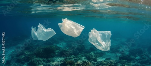 Three plastic bags drift in the azure ocean, blending with the fluid and electric blue water. Life underwater suffers from our aquatic plastic problem. © AkuAku