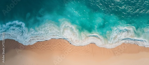 An artistic aerial view showcasing azure waves crashing on a sandy beach, creating a mesmerizing pattern of liquid in an electric blue landscape.