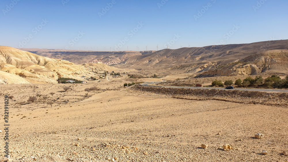 Scenic panoramic view of mountainous desert terrain with wind turbine farm in distance in Jordan, Middle East
