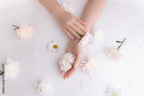 Closeup beautiful sophisticated female hands with pink flowers on white background. Concept hand care, antiwrinkles, antiaging cream, spa photo