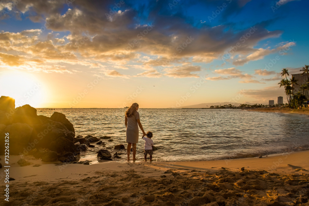 Woman and her son walking together on a beautiful sunset beach in Hawaii. Wide horizontal photo near Honolulu. Family Vacation concept photo. Taking kids on tropical vacations