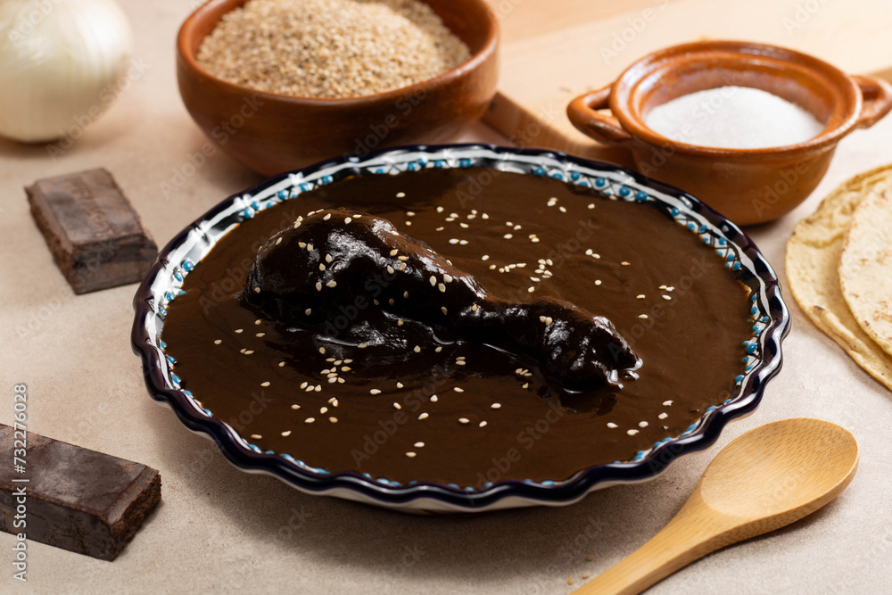 Fototapeta premium Talavera and clay dish filled with black mole, accompanied by tortillas and sesame seeds, on a cement background in Oaxaca