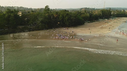 Aerial view of children in white uniforms playing by sea shore at sunset, kids enjoying beach activities, youth gathering coastline, school summer camp fun, outdoors joy, waves meeting sand.